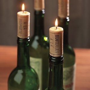 Cork candles lit in green glass wine bottles on a wooden surface, creating a warm and cozy ambiance.