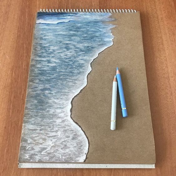 A drawing of a shoreline on a spiral-bound sketchpad with two colored pencils, one white and one blue, placed on the sketchpad.