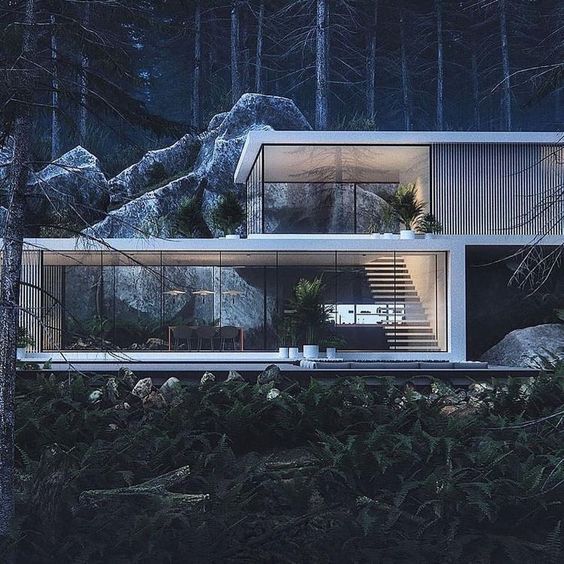 A modern, glass-walled house nestled in a forest at night, with an illuminated interior featuring a dining area and a staircase.