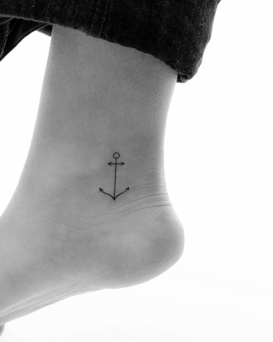 Minimalist anchor tattoo on an ankle, symbolizing stability and strength. Black ink fine-line tattoo design on the side of the foot.