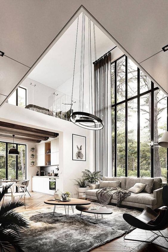 Modern living room with large windows, cozy seating, hanging lights, and loft kitchen in a forest setting. Elegant interior design.