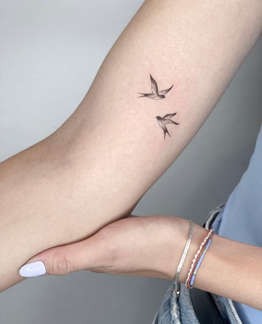 Minimalist bird tattoo on forearm, with two flying birds, simple design, delicate ink art on skin, close-up image.
