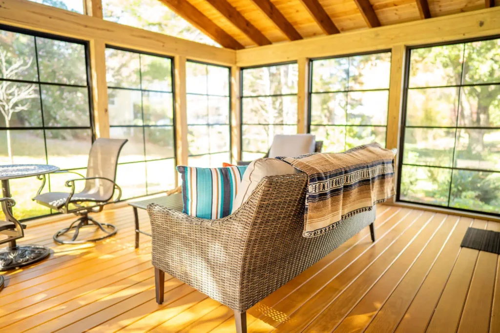 Bright and cozy sunroom with wicker furniture, vibrant pillows, and large windows offering scenic garden views.