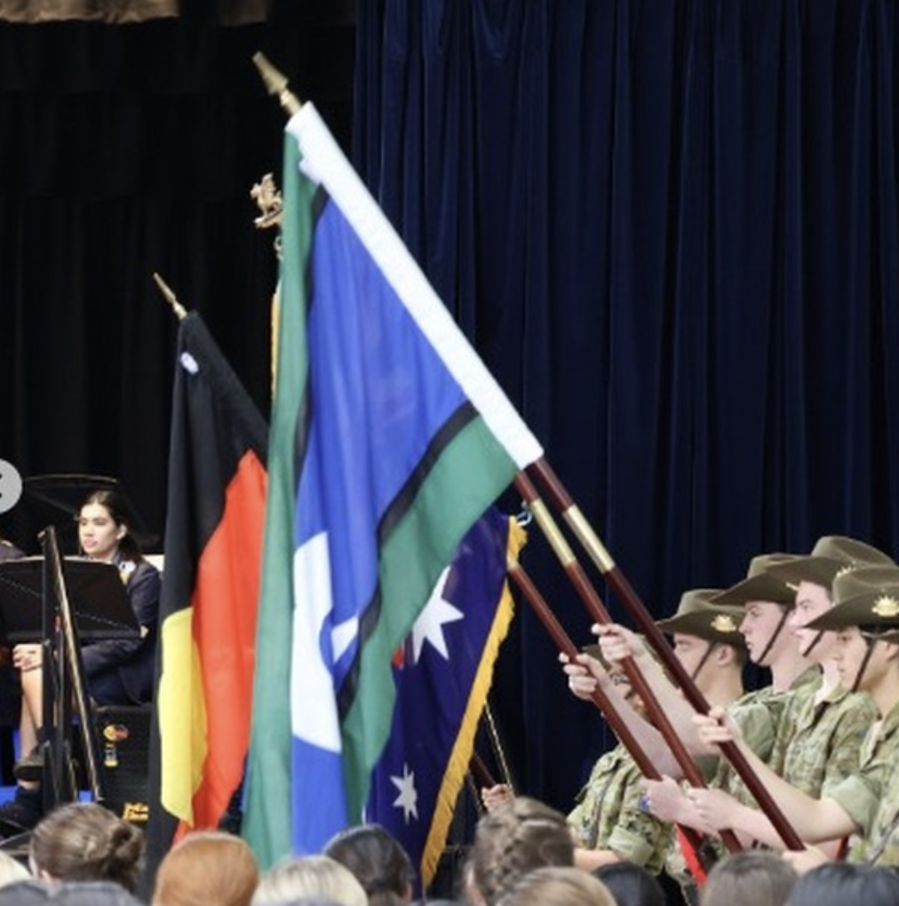 Australian students participate in a ceremony with national and Aboriginal flags, highlighting cultural diversity and unity.