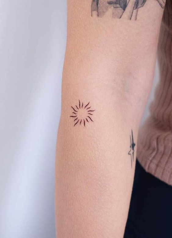 Minimalist sun tattoo on inner forearm with additional small star tattoos, showcasing simple and elegant ink designs.