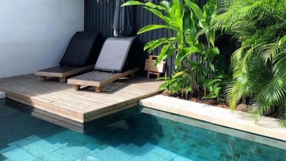 Two lounge chairs beside a tranquil swimming pool in a lush, tropical garden, perfect for relaxation and sunbathing.