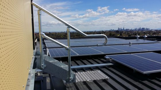 Rooftop solar panels with safety railing and city skyline in the background under a blue sky. Sustainable energy setup.