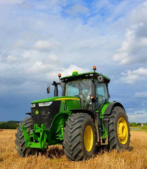 Green tractor on a harvested field under a cloudy sky, ideal farming equipment for agriculture and rural work.