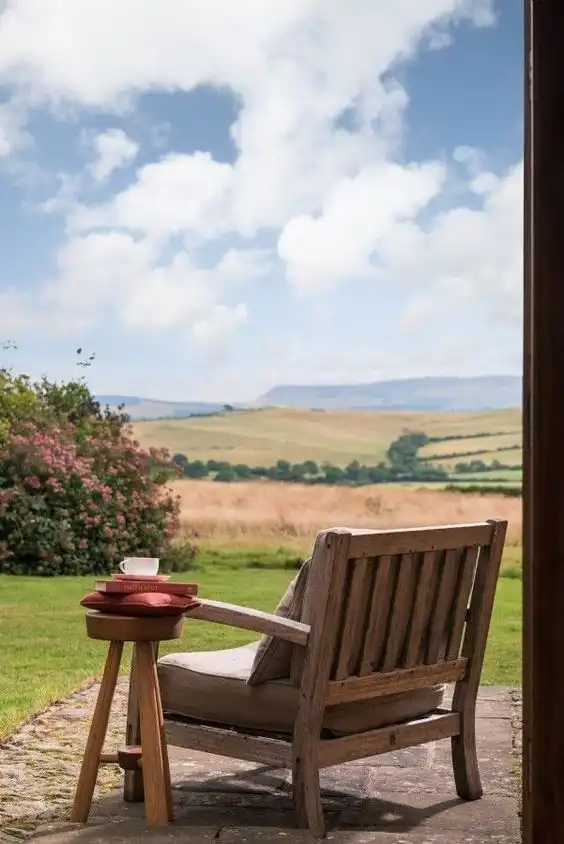 a27908bd621622f42d99e6af46f53086 Cozy wooden chair with a side table holding a cup and books, overlooking a picturesque countryside landscape under a blue sky. | Sky Rye Design Cozy wooden chair with a side table holding a cup and books, overlooking a picturesque countryside landscape under a blue sky.