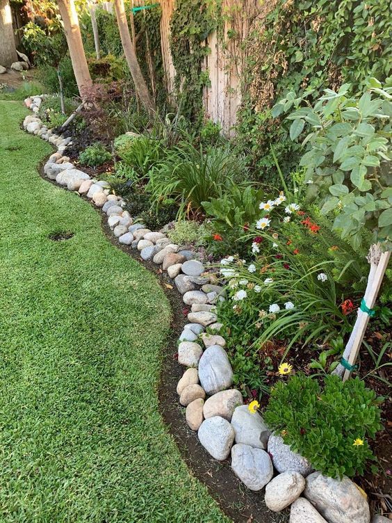 Beautiful garden with stone border, vibrant flowers, lush greenery, and well-manicured lawn. Ideal outdoor landscaping.