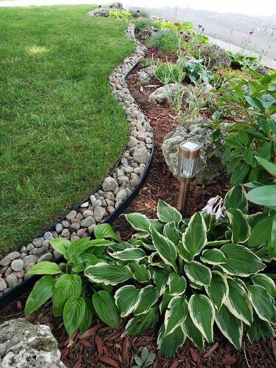 Beautiful garden landscape with green grass, stone border, decorative plants, and solar path light.