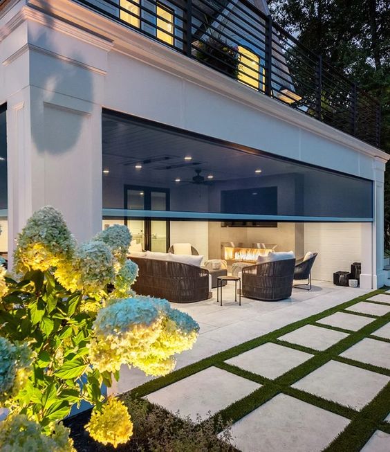 Modern outdoor living space with cozy seating, a built-in fireplace, and elegant garden landscaping with white flowers.