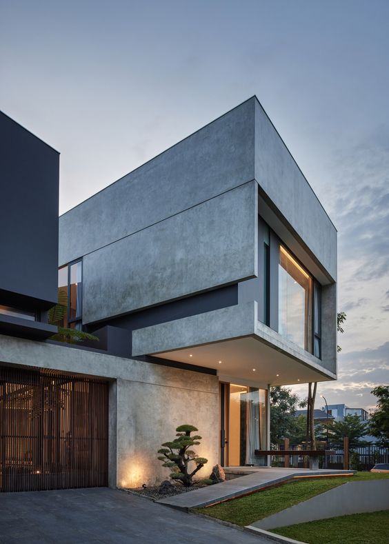 Modern minimalist concrete house exterior with large windows and sleek design, set against a twilight sky.