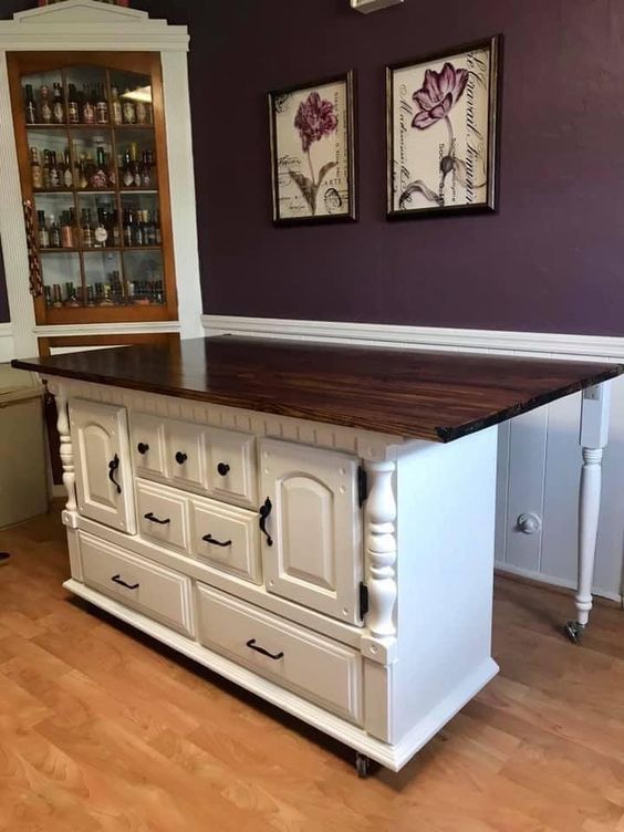 Vintage kitchen island with white cabinets and dark wooden countertop, displayed in a cozy room with wood flooring.