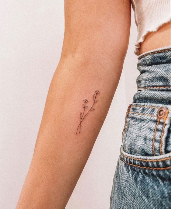 Minimalist floral tattoo on a person's inner forearm, wearing high-waisted denim jeans and a white top.