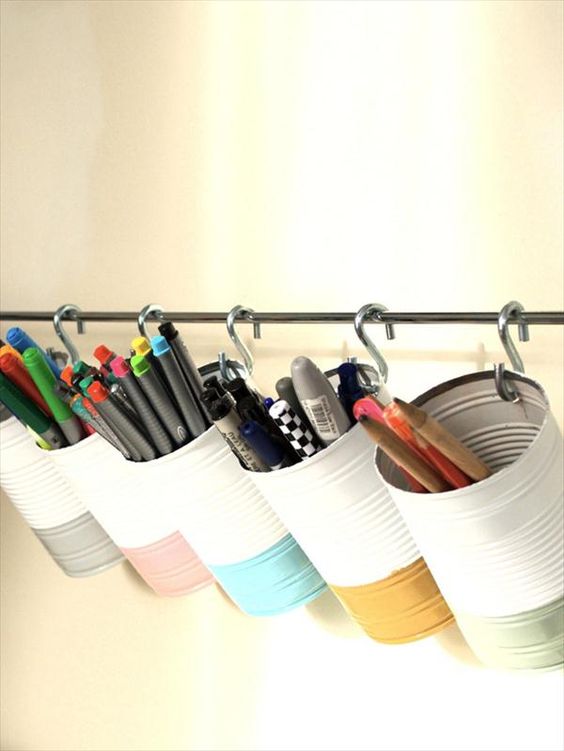 DIY pen and marker holder made from upcycled tin cans, neatly arranged on a rod with hooks for organized desk storage.