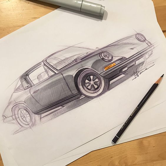 Hand-drawn sketch of a vintage sports car with pencils and markers on a wooden table. Detailed rendering and signature visible.