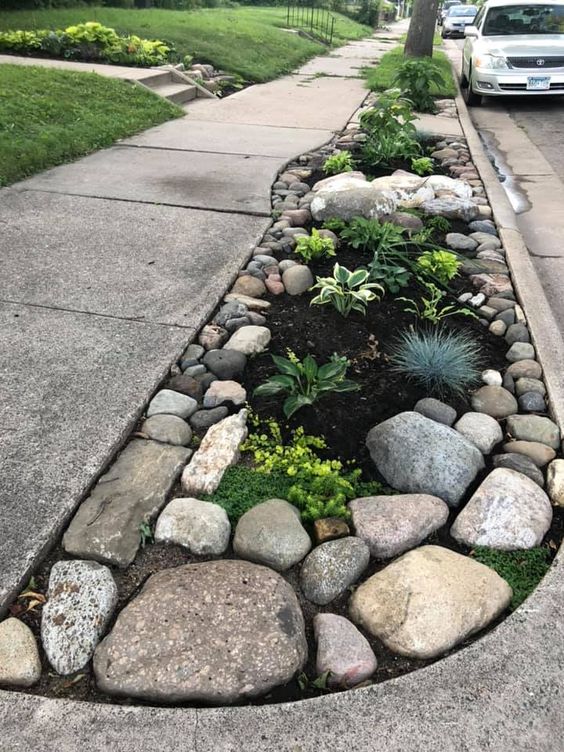 Beautiful roadside rock garden with lush greenery and a variety of stones on an urban sidewalk.