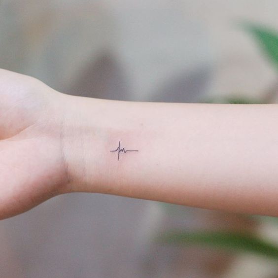 Minimalist heartbeat wrist tattoo on a person's forearm, symbolizing life and vitality, against a blurred background.