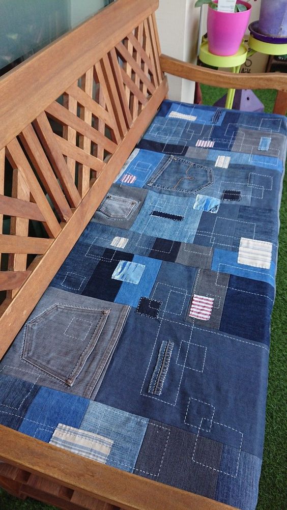 Wooden bench with a patchwork denim cushion, featuring various shades of blue and small colorful patches.