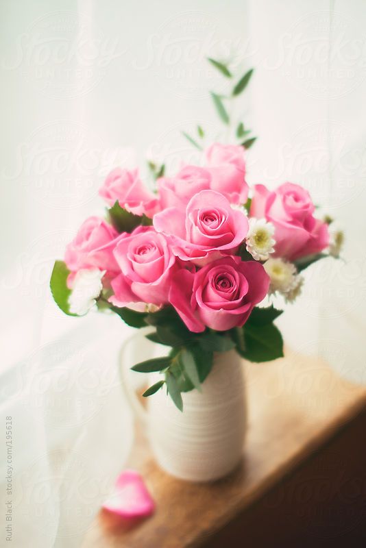 Vibrant pink roses in a white vase on a wooden table, brightening a cozy room with natural light streaming through the window.