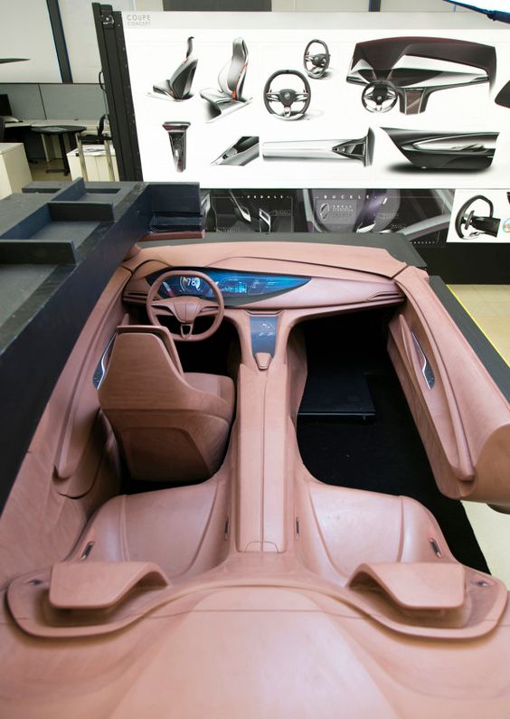 Clay model of futuristic car interior with steering wheel and dashboard design sketches in the background.