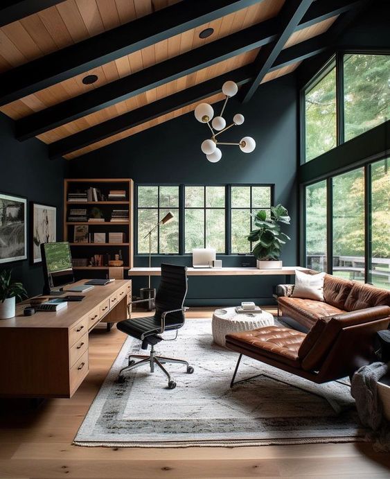 Modern home office with large windows, black walls, wooden desk, leather sofa, stylish rug, and mid-century furniture.