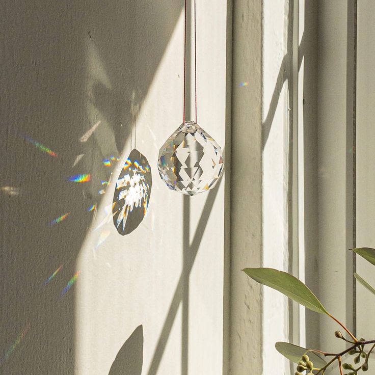 Hanging crystal prism casting colorful light reflections on white wall near sunlit window.