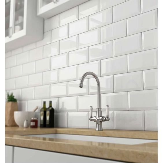 Modern kitchen with glossy white subway tile backsplash, sleek faucet, and beige countertop. Ideal for contemporary home decor.