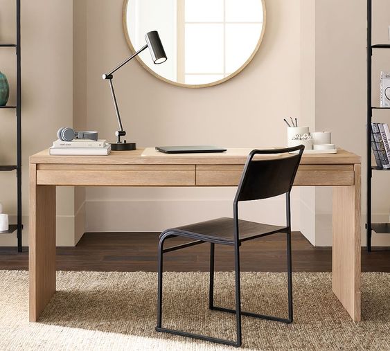 Modern wooden desk with a black chair, desk lamp, and office supplies in a stylish home office setup with neutral tones.