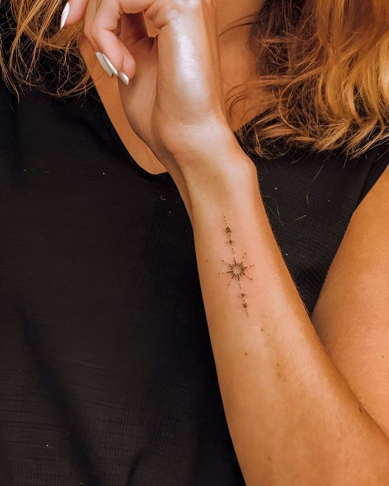 Woman with a small compass and constellations tattoo on her inner forearm, wearing a black sleeveless top.