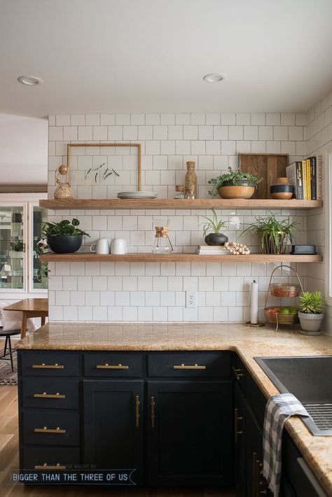 Modern kitchen with black cabinets, open wooden shelves, white subway tiles, and natural decor elements, including plants and ceramics.