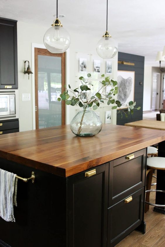 Modern kitchen with a wooden island top, black cabinets, pendant lights, and a glass vase with eucalyptus branches.