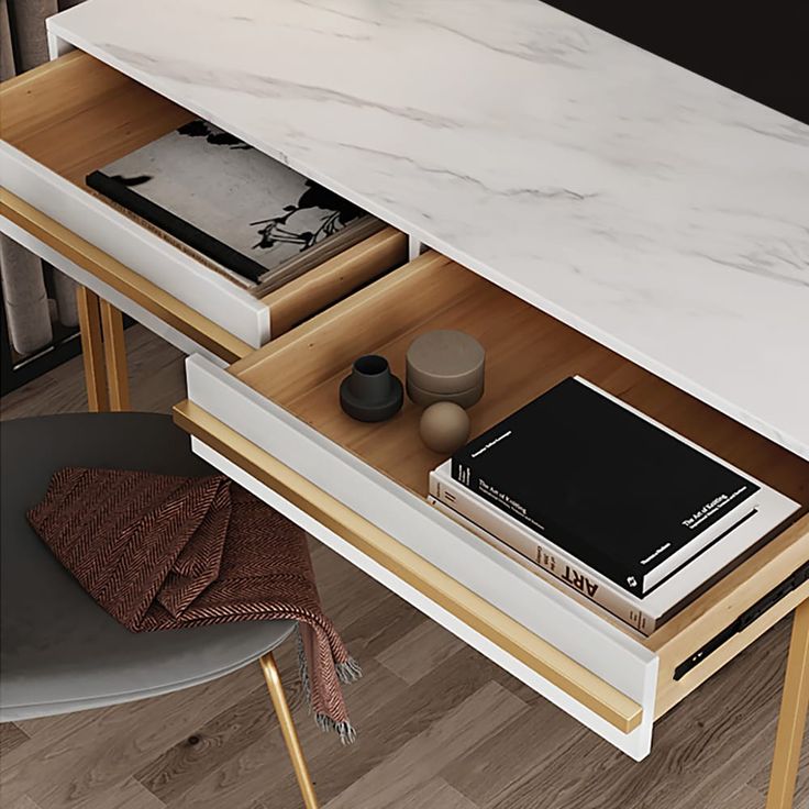 Modern white marble desk with open wooden drawers, featuring black book, decor items, and a grey chair.