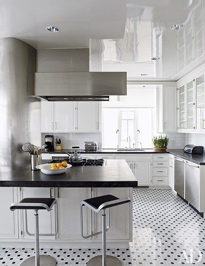 Modern white kitchen with stainless steel appliances, black countertops, and polka-dot tile floor with bar stools and island.