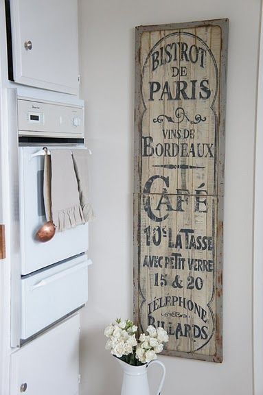 Vintage French kitchen decor with Bistrot de Paris wall sign, white cabinets, oven, and a pitcher of white flowers.