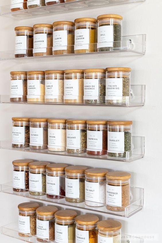 Organized spice rack with labeled glass jars containing various spices like paprika, dill, cumin, and more in a kitchen.