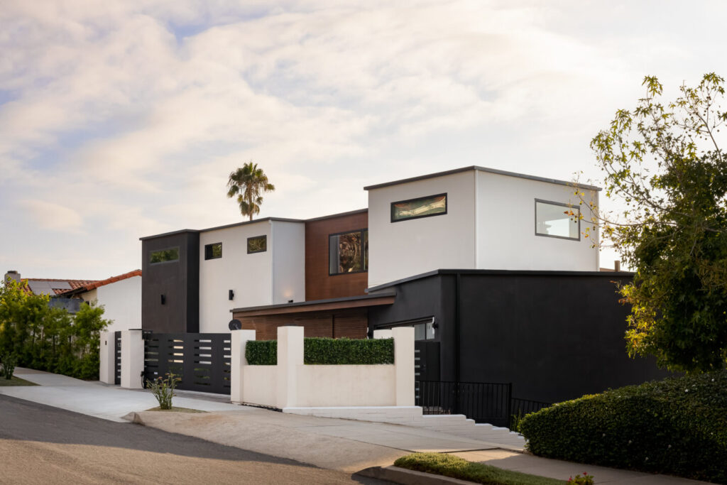 Modern two-story home with sleek black and white exterior, large windows, and landscaped front yard on a sunny day.