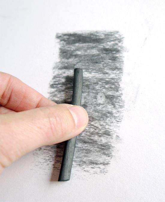 Hand shading with charcoal stick on white paper, creating texture for art and drawing.