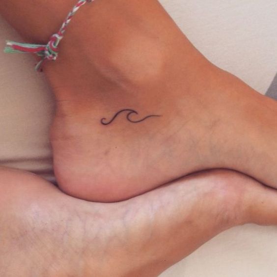 Minimalist wave tattoo on ankle, paired with a colorful friendship bracelet, showcasing a simple and elegant foot design.