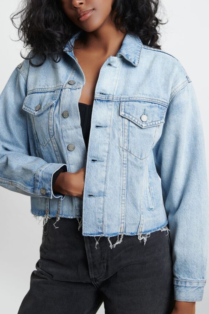 Woman in a cropped denim jacket and black pants, showing casual and trendy fashion style. Close-up torso view.