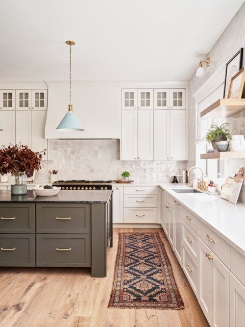 Bright farmhouse kitchen with white cabinets, green island, pendant lights, and rustic rug on wooden floor.