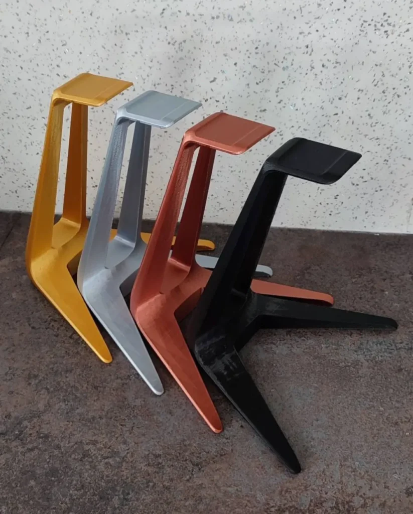 Colorful 3D printed headset stands in gold, silver, red, and black, organized in a leaning stack on a textured surface.