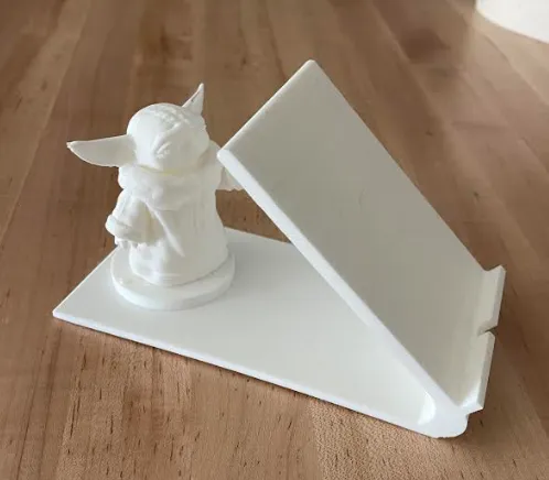 3D-printed Yoda-themed phone stand on wooden table, perfect for holding smartphones or small devices securely.