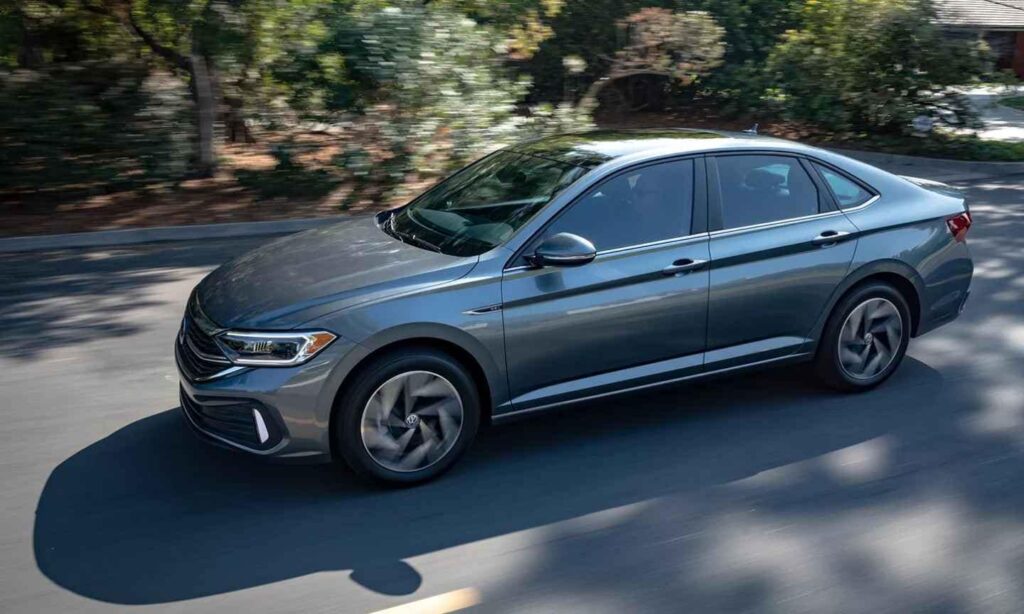 A sleek grey sedan driving on a tree-lined street in daylight.