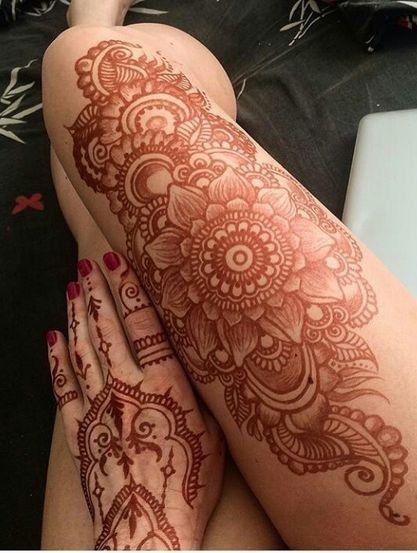 Detailed henna designs on a person's hand and full leg, showcasing intricate floral and paisley patterns.