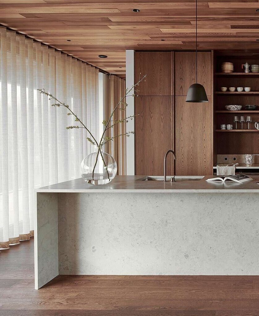 Modern kitchen design with wooden elements, marble island, pendant light, and vase with branches on countertop.