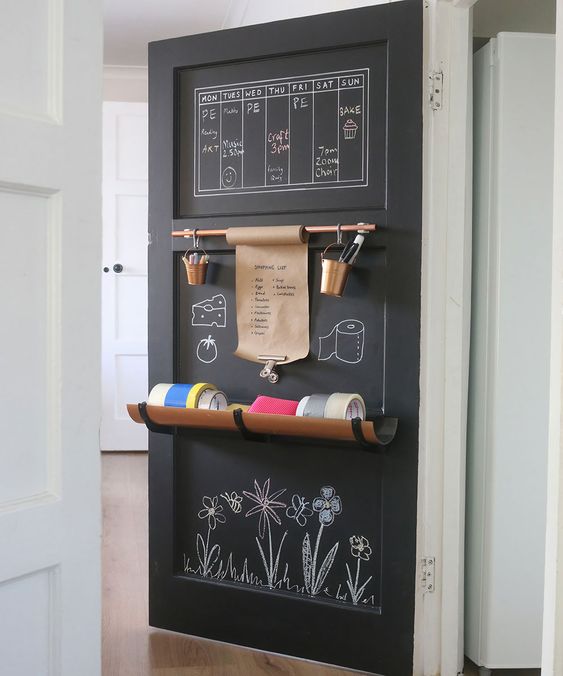 Chalkboard door organizer with weekly plans, copper buckets, shopping list, tape rolls, and flower chalk drawings.