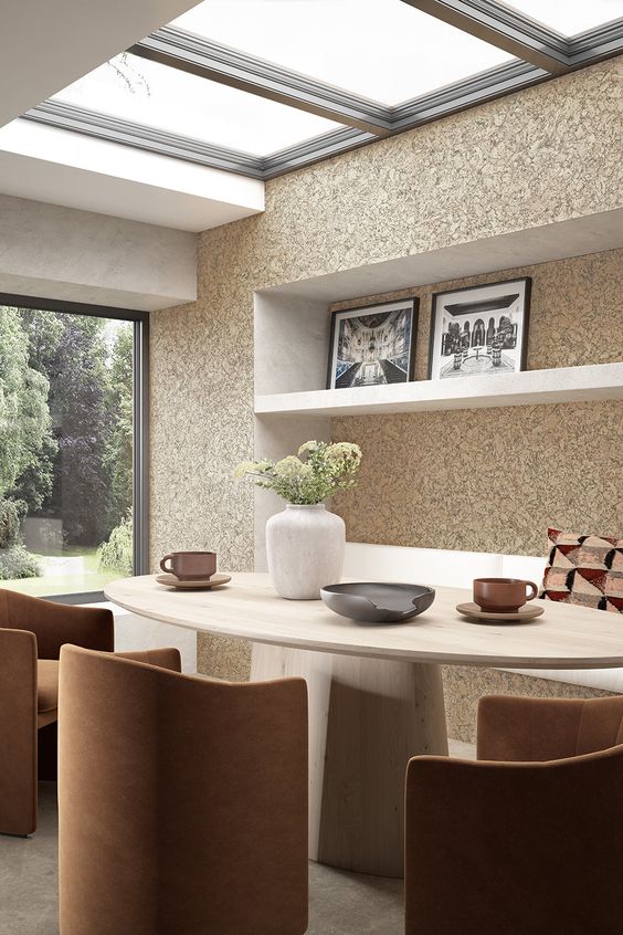 Modern dining room with skylight, oval table, brown chairs, green plants, wall art, and garden view through large window.