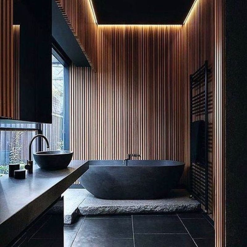 Modern bathroom with a sleek black bathtub, wooden panel walls, ambient lighting, and a stylish black sink.